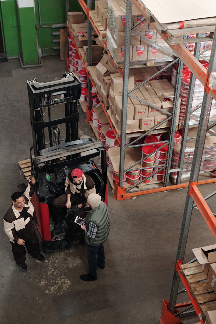gallery-05 High-angle view of warehouse employees operating a forklift surrounded by stacked shelves.